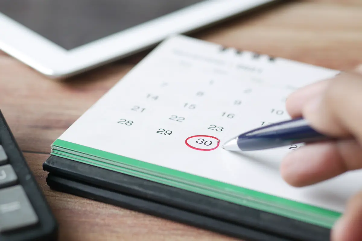 Hand holding a pen beside a circled date on a desk calendar