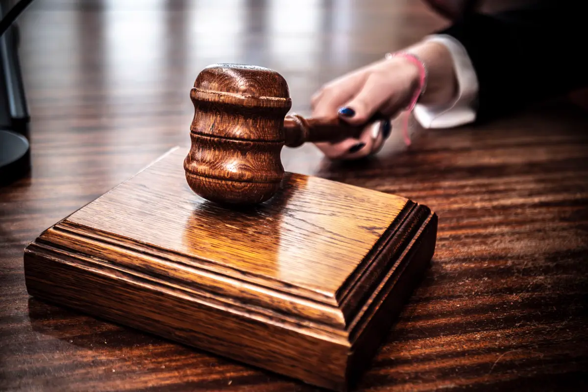 Wooden gavel on a courtroom desk with a hand in the background